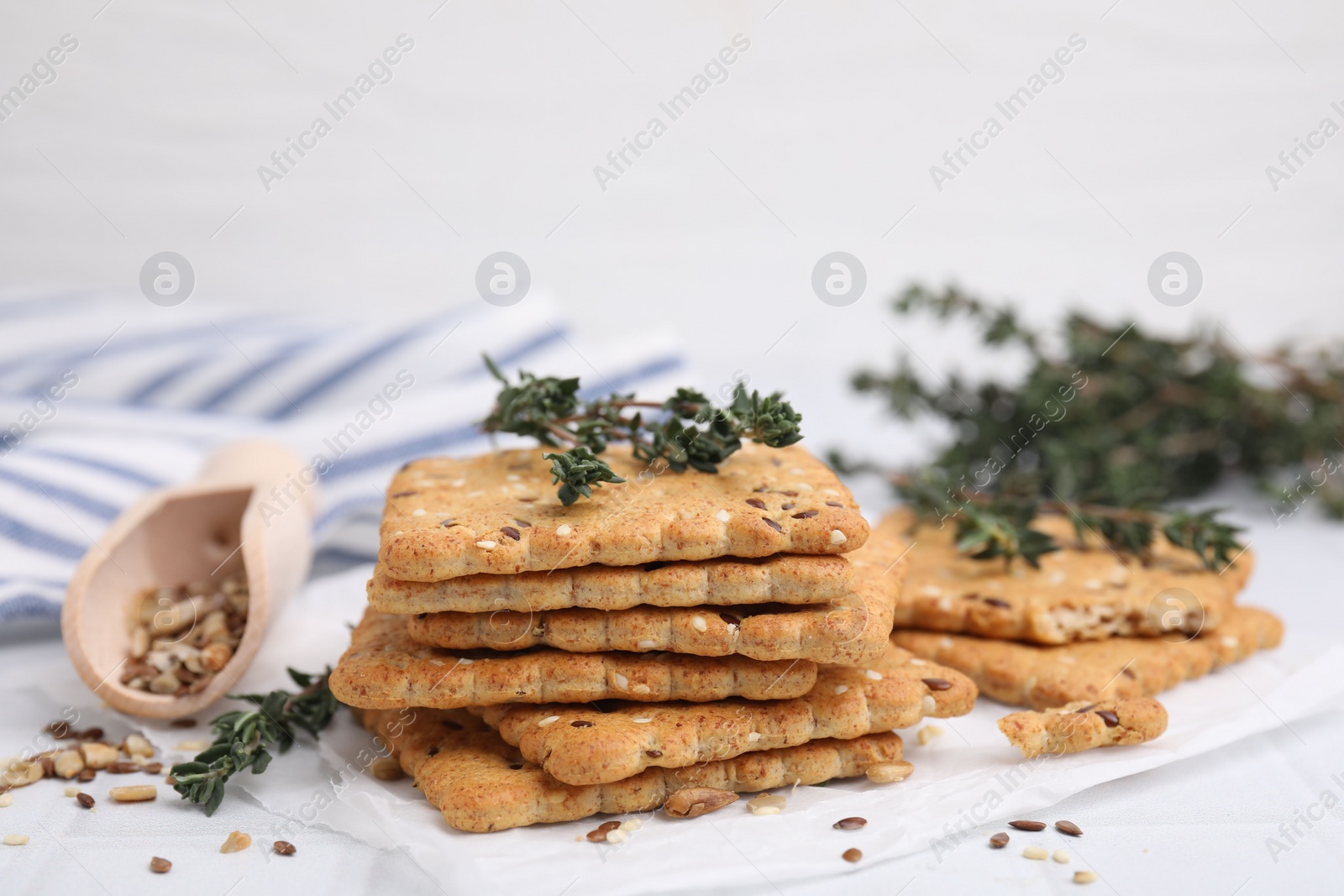 Photo of Cereal crackers with flax, sesame seeds and thyme on white tiled table, closeup