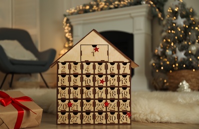 Wooden house shaped Advent calendar and gift box in room decorated for New Year