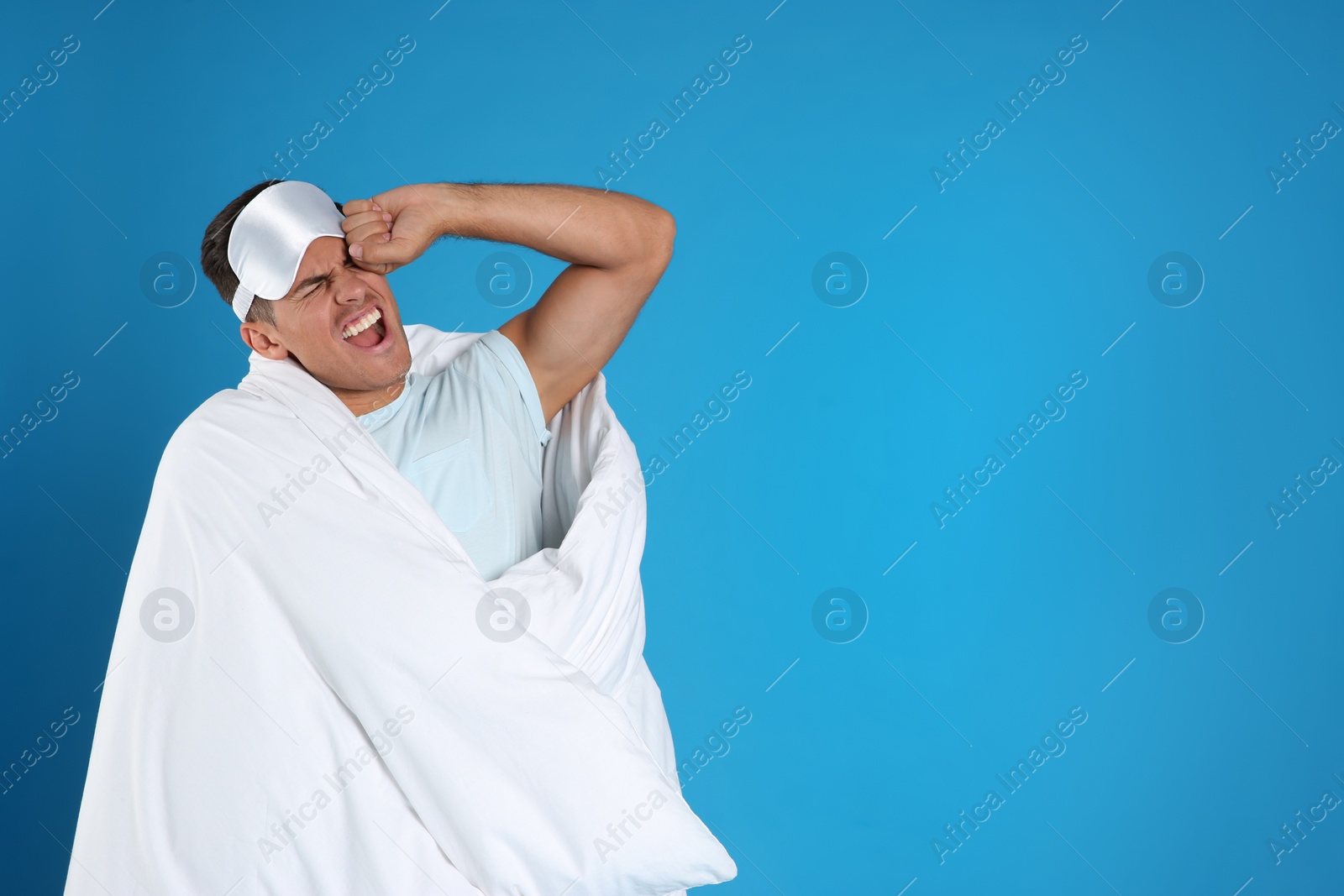 Photo of Man wrapped in blanket yawning on blue background. Space for text