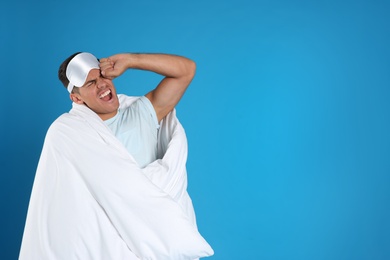 Photo of Man wrapped in blanket yawning on blue background. Space for text