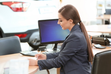 Photo of Young saleswoman sitting at table in car salon
