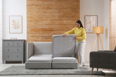 Photo of Young woman unfolding sofa into a bed in room. Modern interior