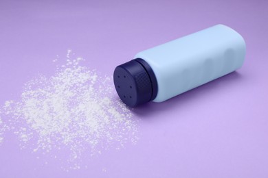 Bottle and scattered dusting powder on violet background. Baby cosmetic product