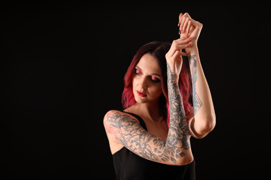 Beautiful woman with tattoos on arms against black background. Space for text