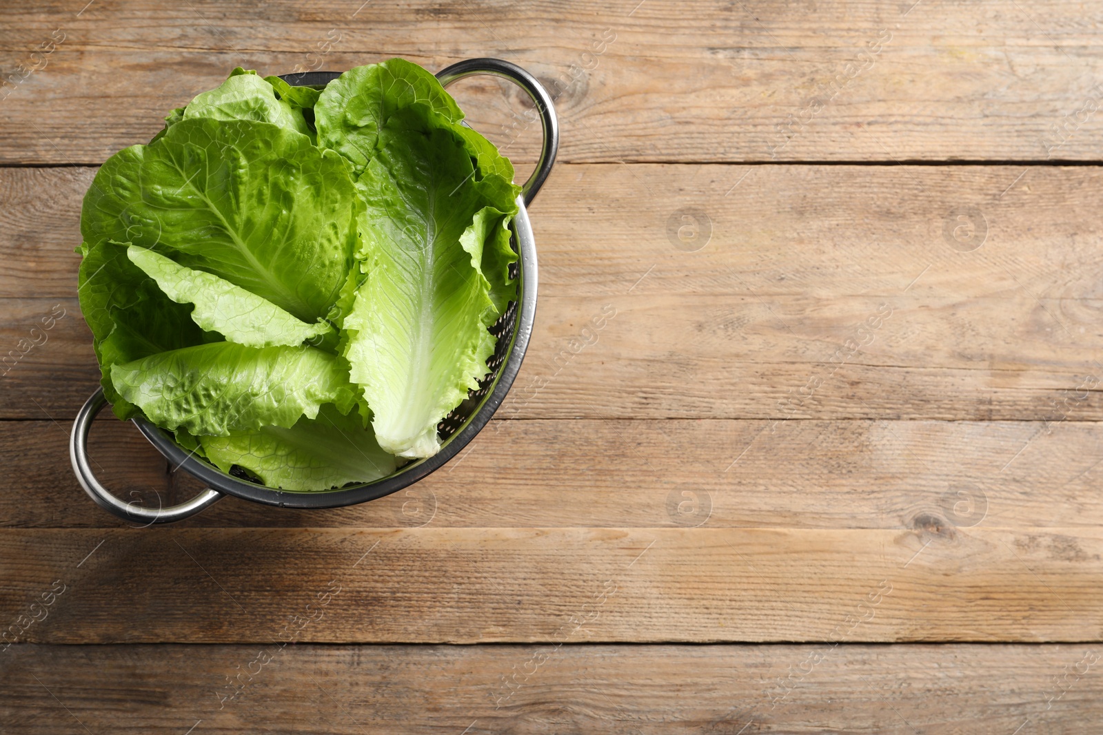 Photo of Colander with fresh leaves of green romaine lettuce on wooden table, top view. Space for text