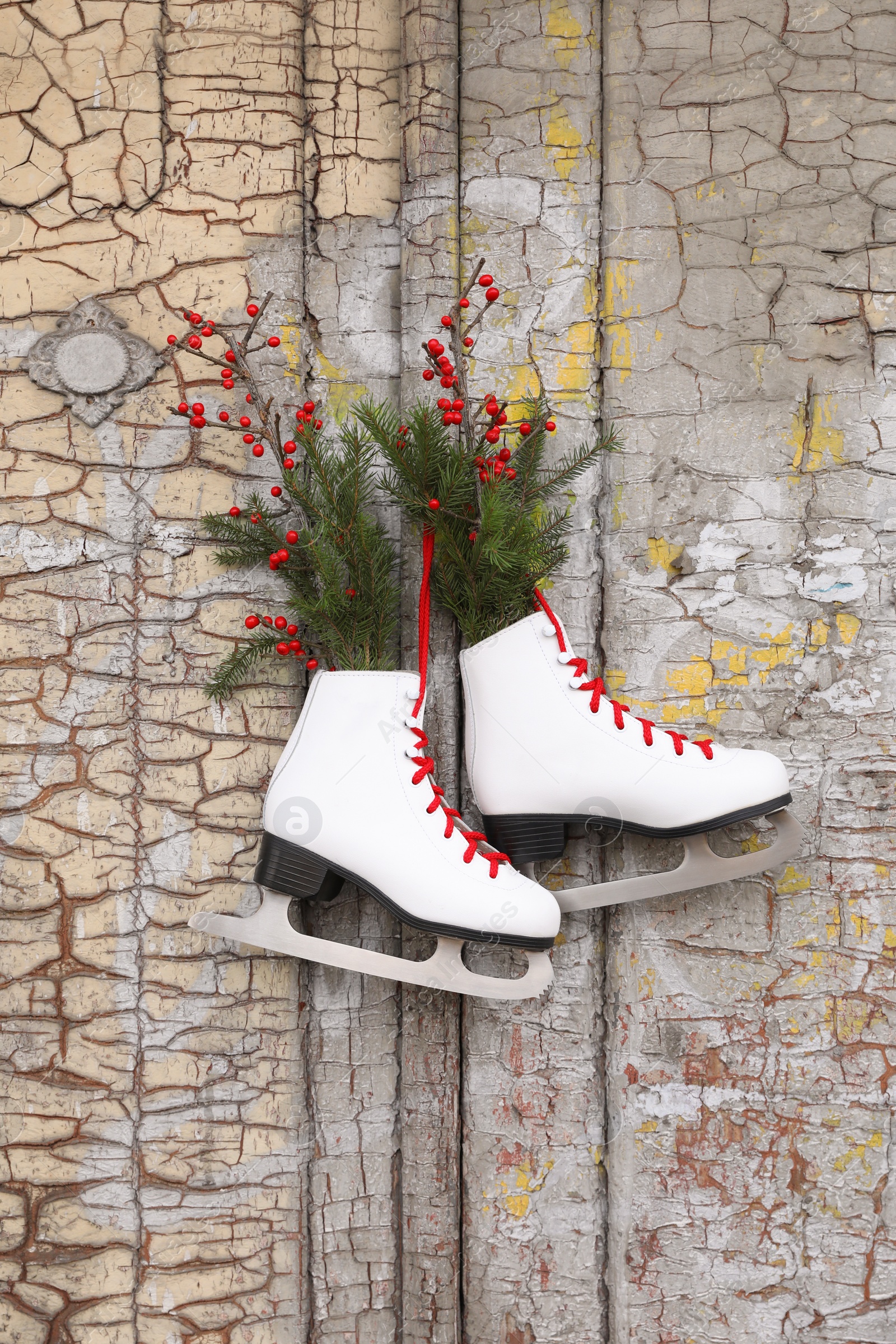 Photo of Pair of ice skates with Christmas decor hanging on old wooden door