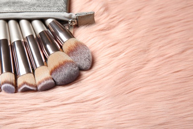 Photo of Bag with set of professional makeup brushes on furry fabric. Space for text