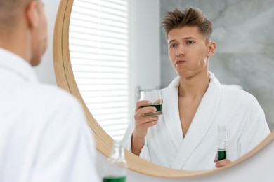 Photo of Young man using mouthwash near mirror in bathroom