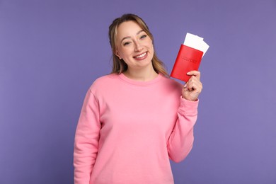 Happy young woman with passport and ticket on purple background