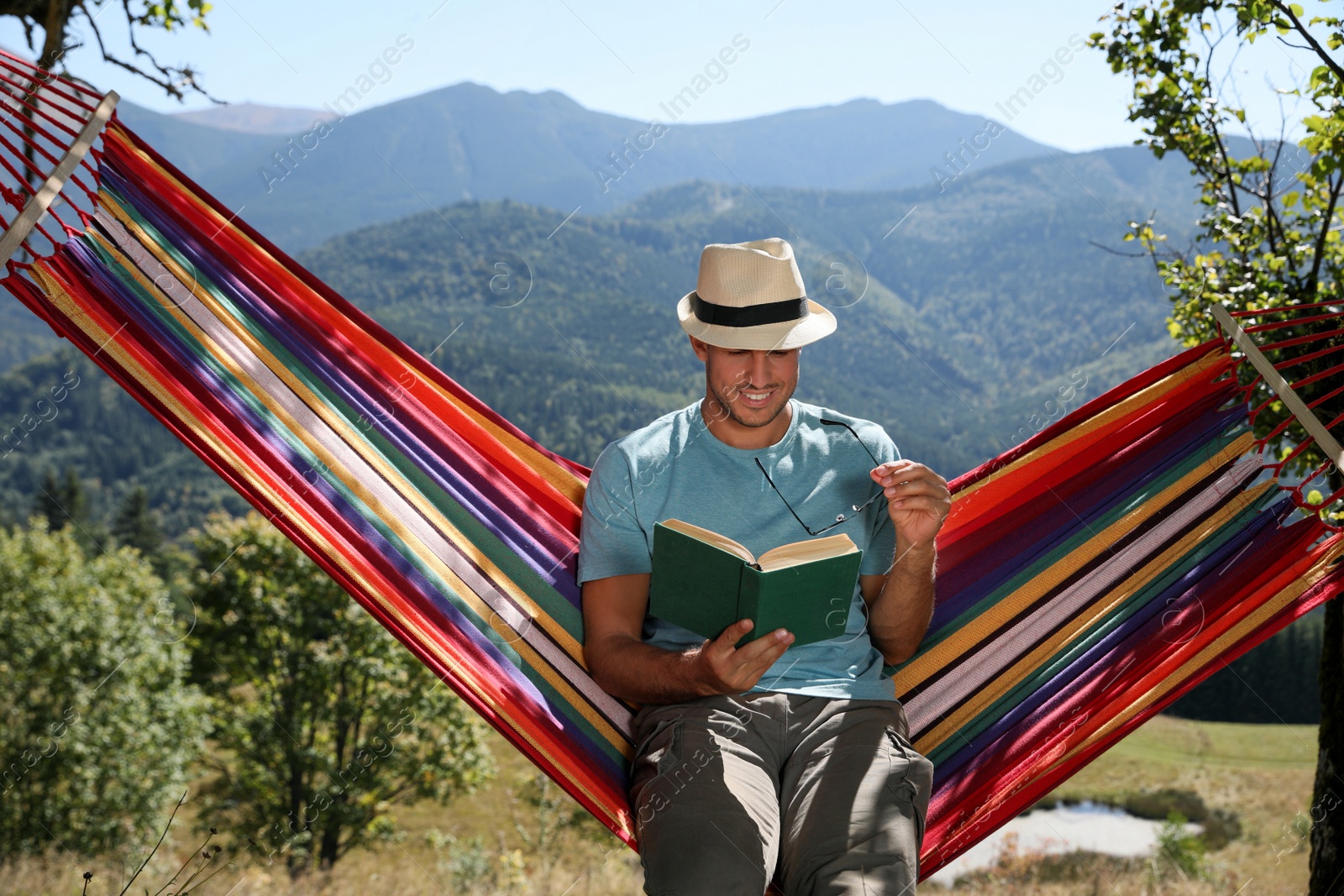 Photo of Handsome man reading book in hammock outdoors on sunny day