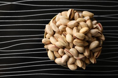 Photo of Many tasty pistachios on black table, top view