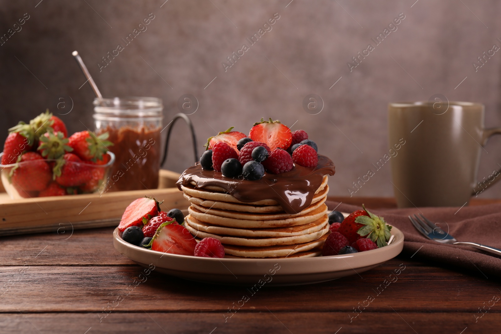 Photo of Stack of tasty pancakes with fresh berries and chocolate spread on wooden table