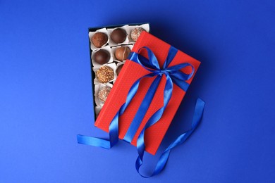 Photo of Box with delicious chocolate candies on blue background, top view