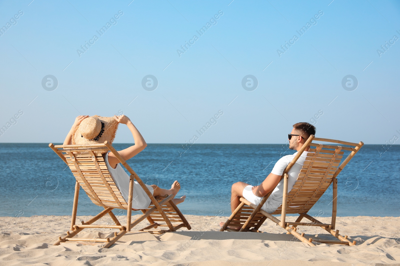 Photo of Young couple relaxing in deck chairs on beach