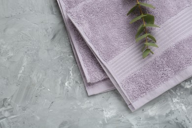 Photo of Violet terry towel and eucalyptus branch on grey table, top view. Space for text