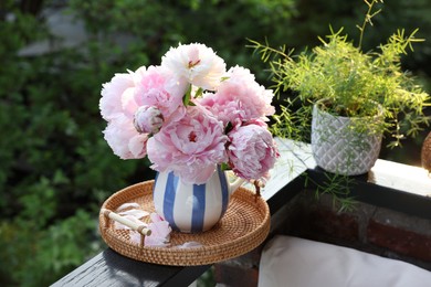 Photo of Beautiful pink peony flowers in vase and potted plant on balcony railing outdoors