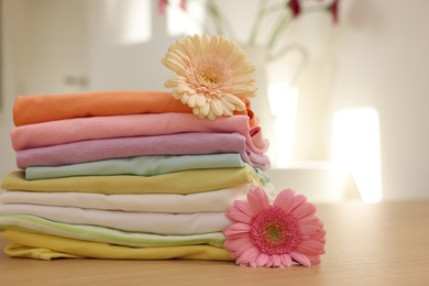 Photo of Stack of clean clothes and flowers on wooden table