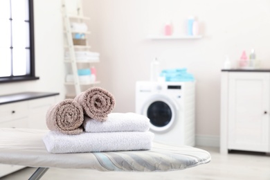 Photo of Soft bath towels on ironing board against blurred background, space for text