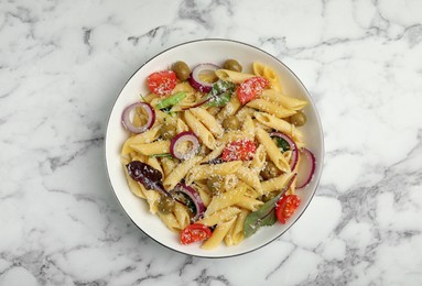 Bowl of delicious pasta with tomatoes, olives and onion on white marble table, top view