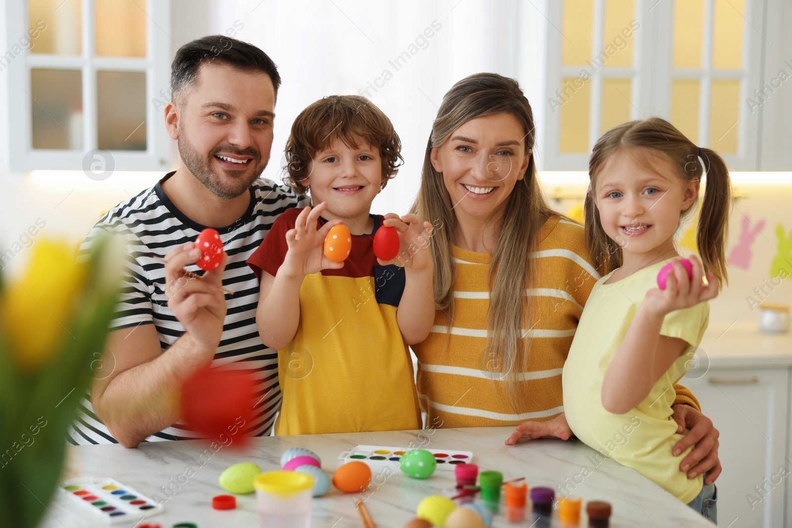 Photo of Easter celebration. Portrait of happy family with painted eggs at white marble table in kitchen