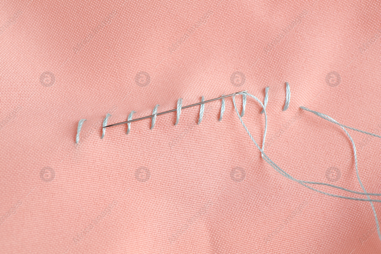 Photo of Sewing needle with thread and stitches on coral cloth, top view