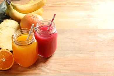 Photo of Different juices in mason jars and fresh fruits on wooden table. Space for text