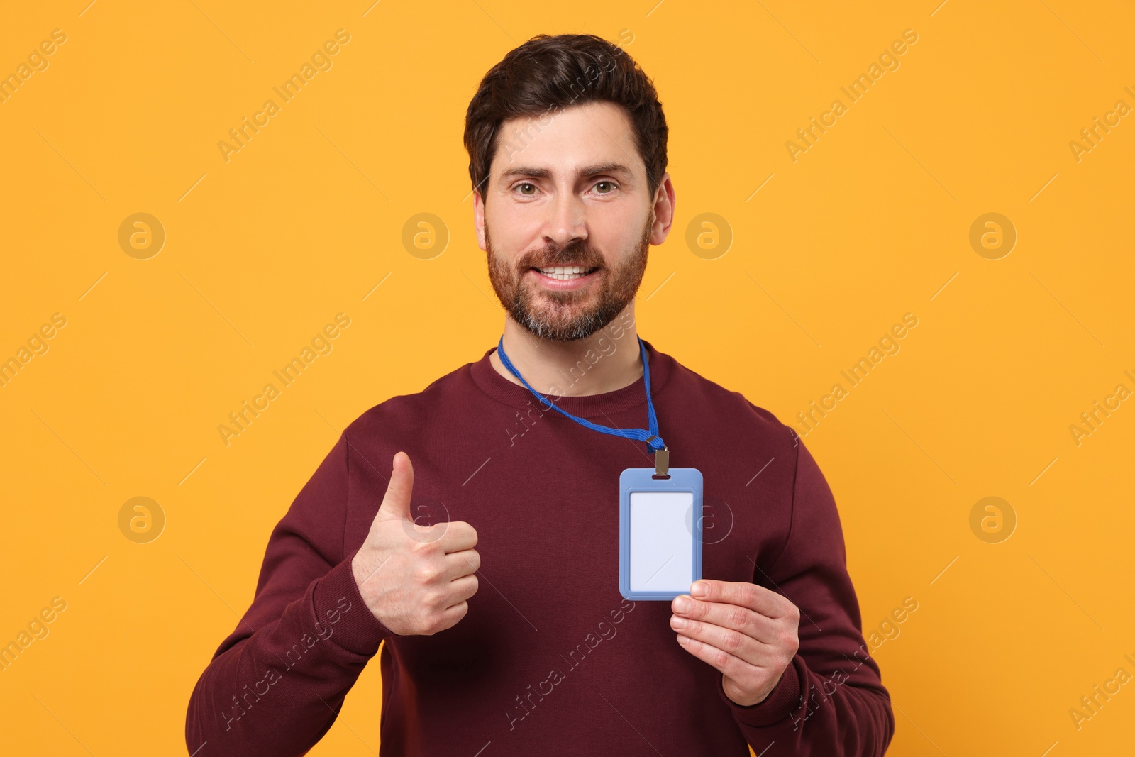 Photo of Smiling man with VIP pass badge showing thumbs up on orange background