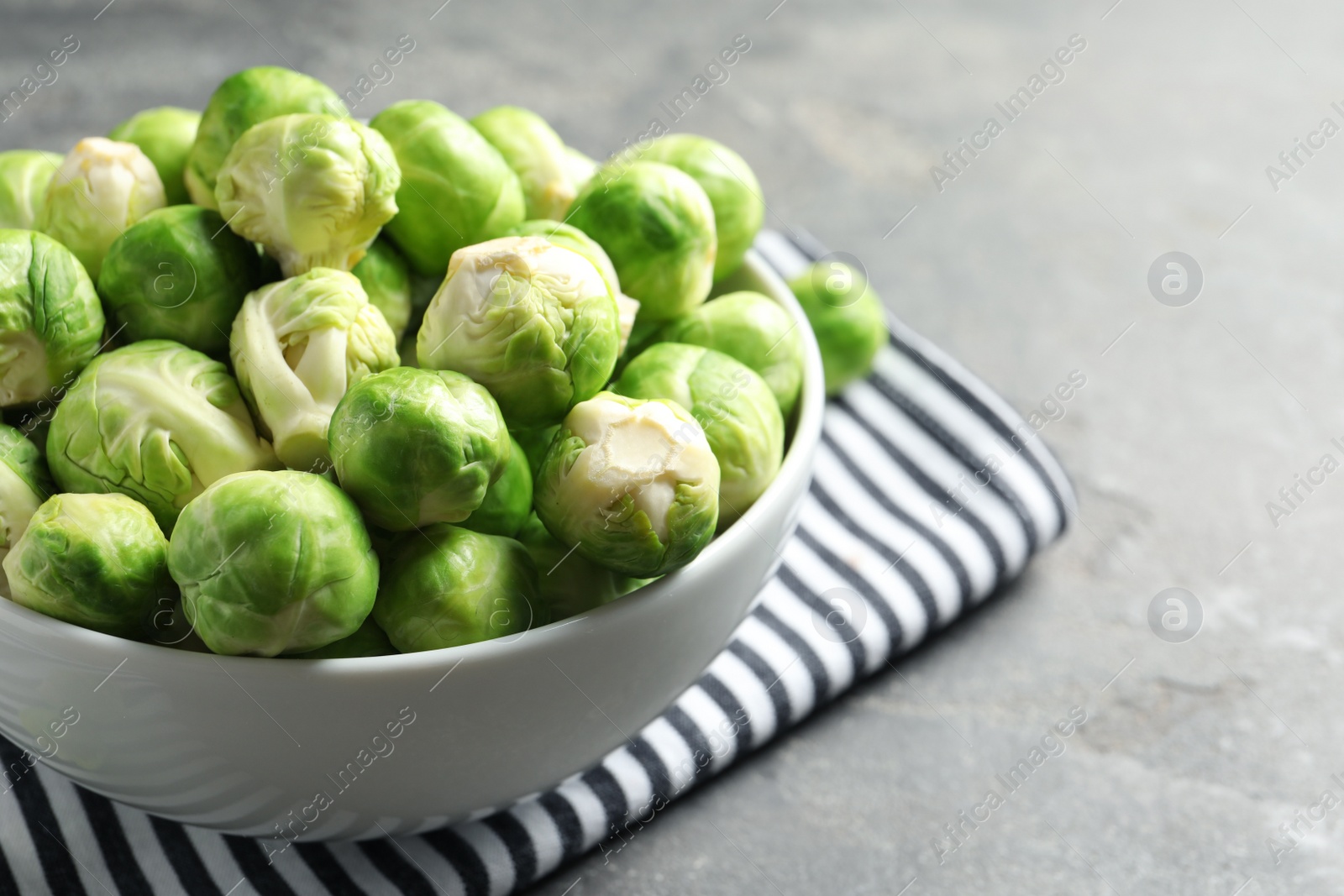 Photo of Bowl of fresh Brussels sprouts and napkin on grey table, closeup. Space for text