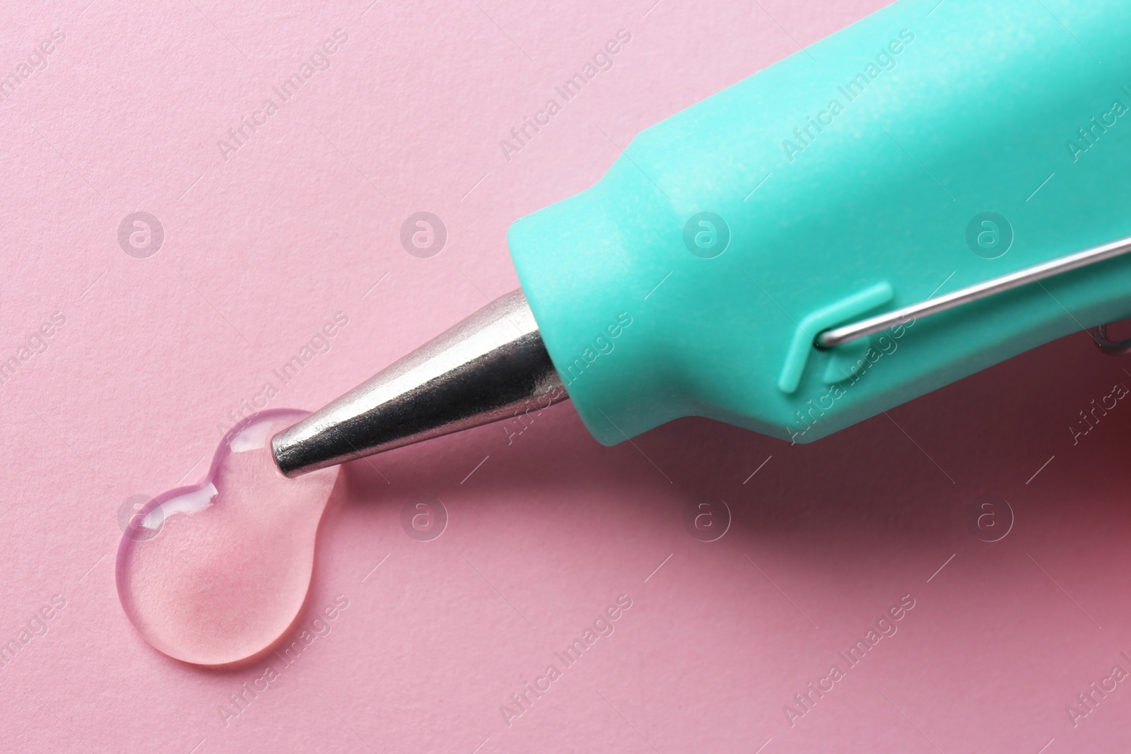 Photo of Melted glue dripping out of hot gun nozzle on pink background, closeup