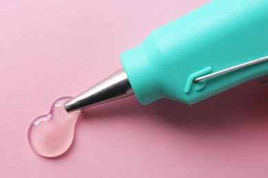 Photo of Melted glue dripping out of hot gun nozzle on pink background, closeup
