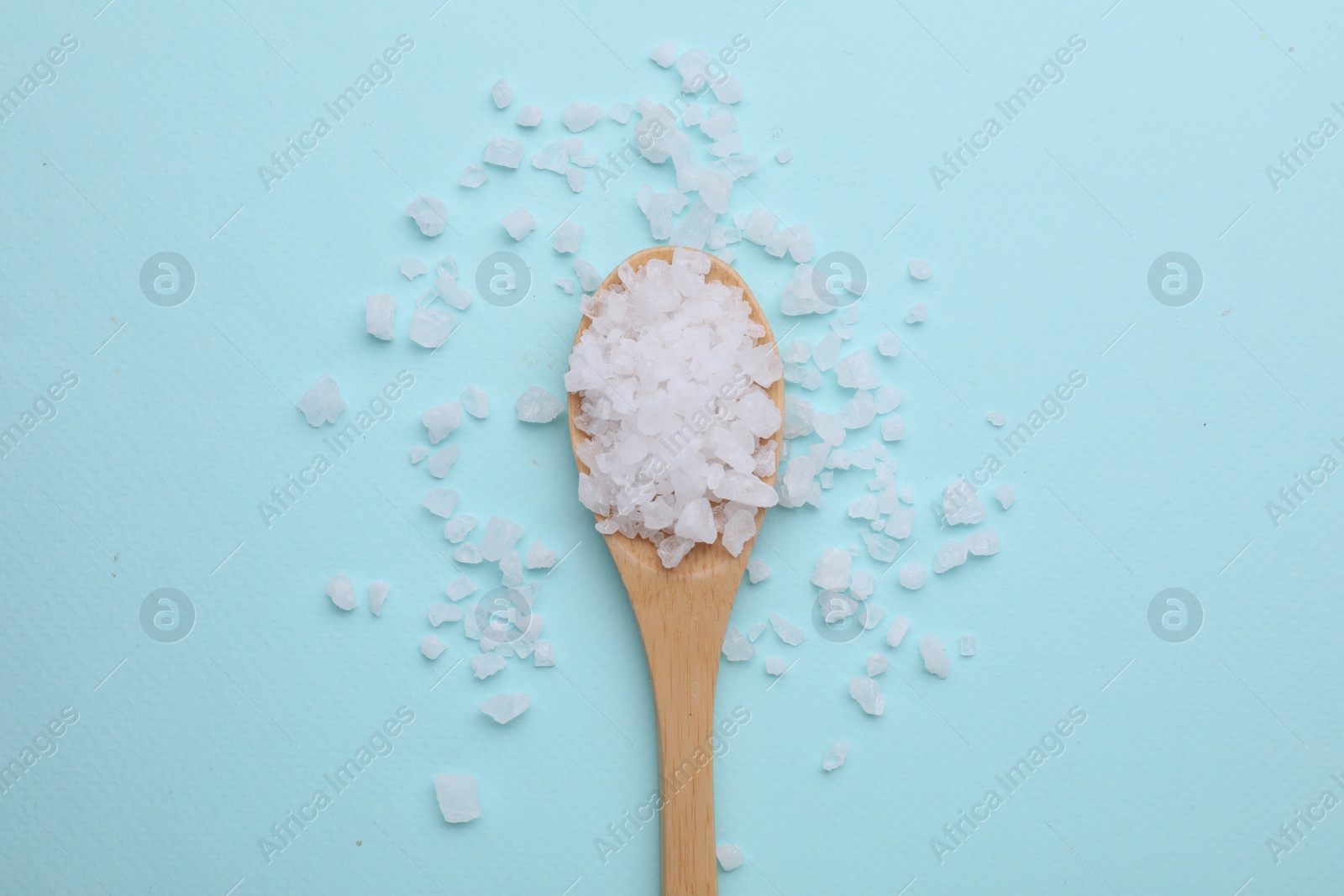 Photo of Spoon with sea salt on light blue background, top view