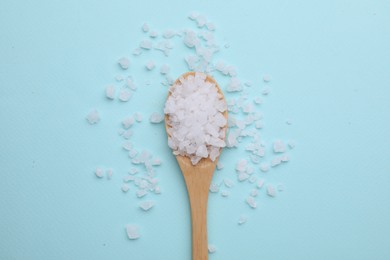 Photo of Spoon with sea salt on light blue background, top view