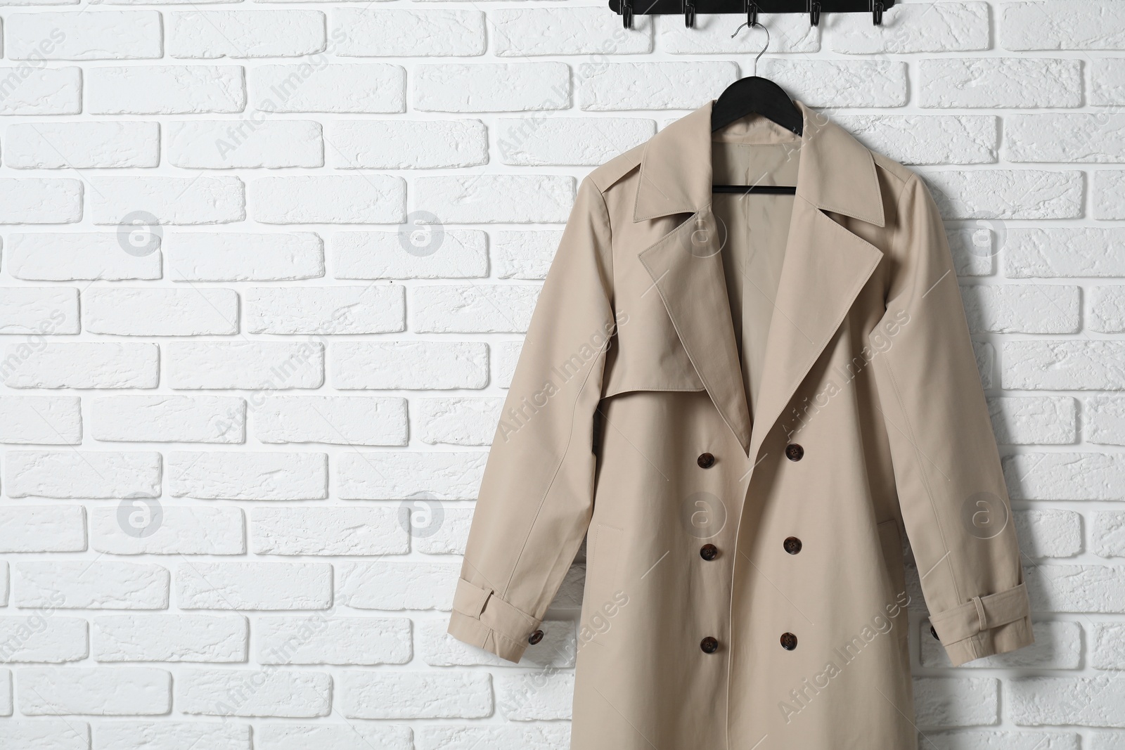 Photo of Hanger with beige coat on white brick wall, space for text