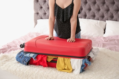 Photo of Young woman struggling to close suitcase on bed