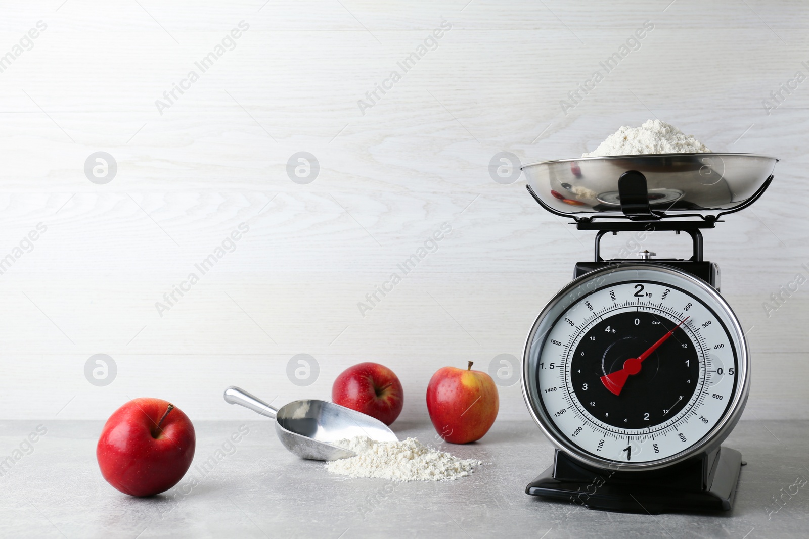 Photo of Kitchen scale with flour and ripe apples on grey table