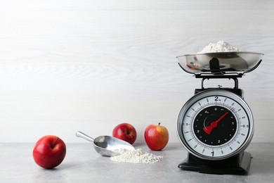 Kitchen scale with flour and ripe apples on grey table