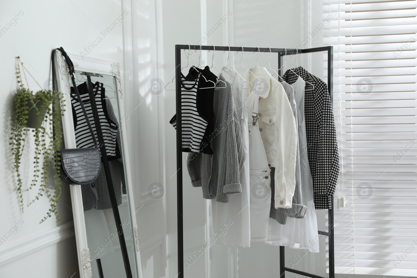 Photo of Rack with stylish women's clothes and large mirror in dressing room. Interior design