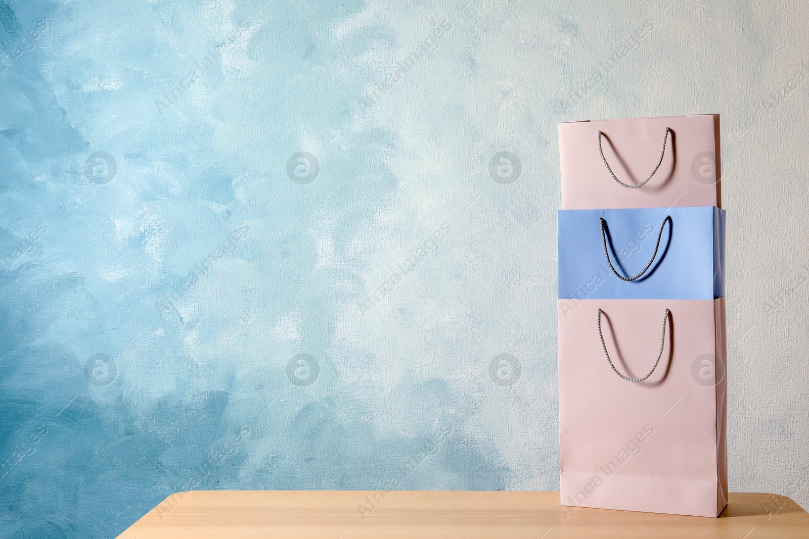 Photo of Colorful paper shopping bags on table against color background. Space for text