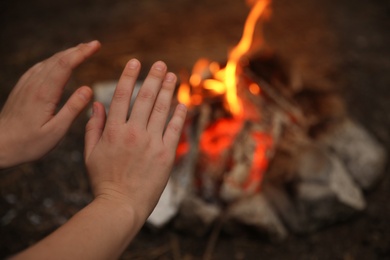 Photo of Woman warming hands near burning firewood outdoors, closeup
