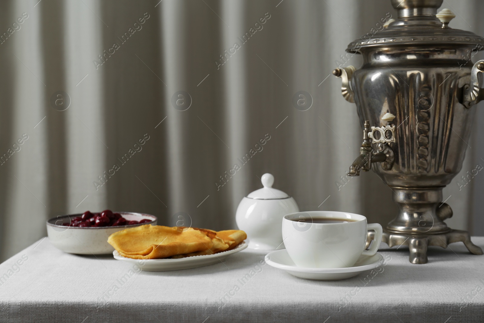 Photo of Vintage samovar, cup of hot drink and snacks served on table indoors. Traditional Russian tea ceremony