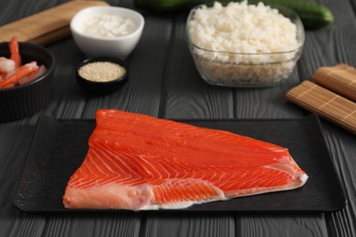 Photo of Making sushi rolls. Fresh salmon and other ingredients on black wooden table, closeup