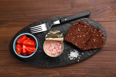 Photo of Can of conserved tuna, tomatoes and bread on wooden table, top view