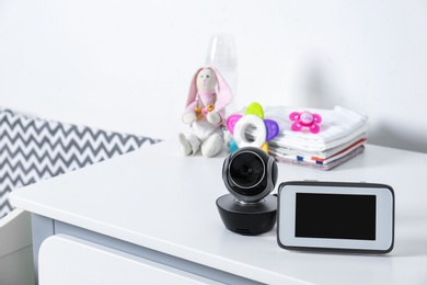 Photo of Baby monitor with camera and accessories on chest of drawers in room, space for text. Video nanny