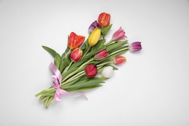 Photo of Bouquet of beautiful colorful tulips tied with pink ribbon on white background, top view