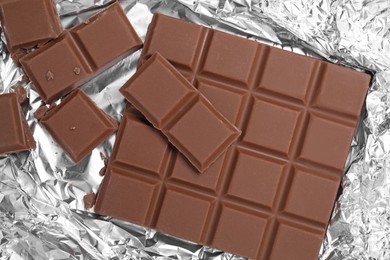 Photo of Pieces of delicious milk chocolate bars on foil, flat lay