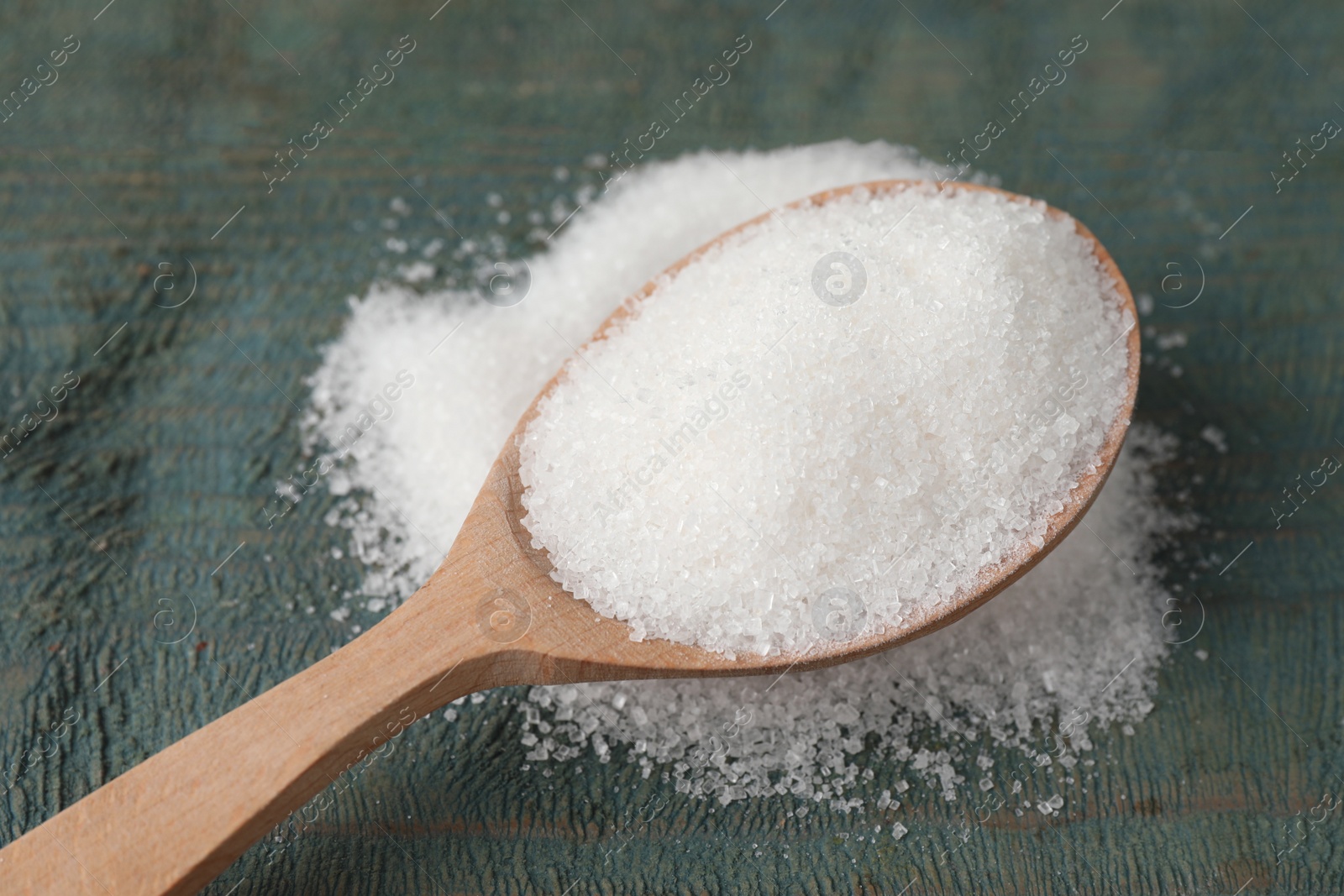 Photo of Spoon with granulated sugar on light blue wooden table, closeup