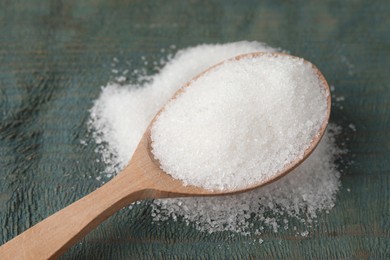 Spoon with granulated sugar on light blue wooden table, closeup