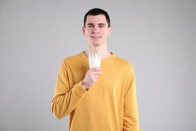 Photo of Happy man with milk mustache holding glass of tasty dairy drink on gray background