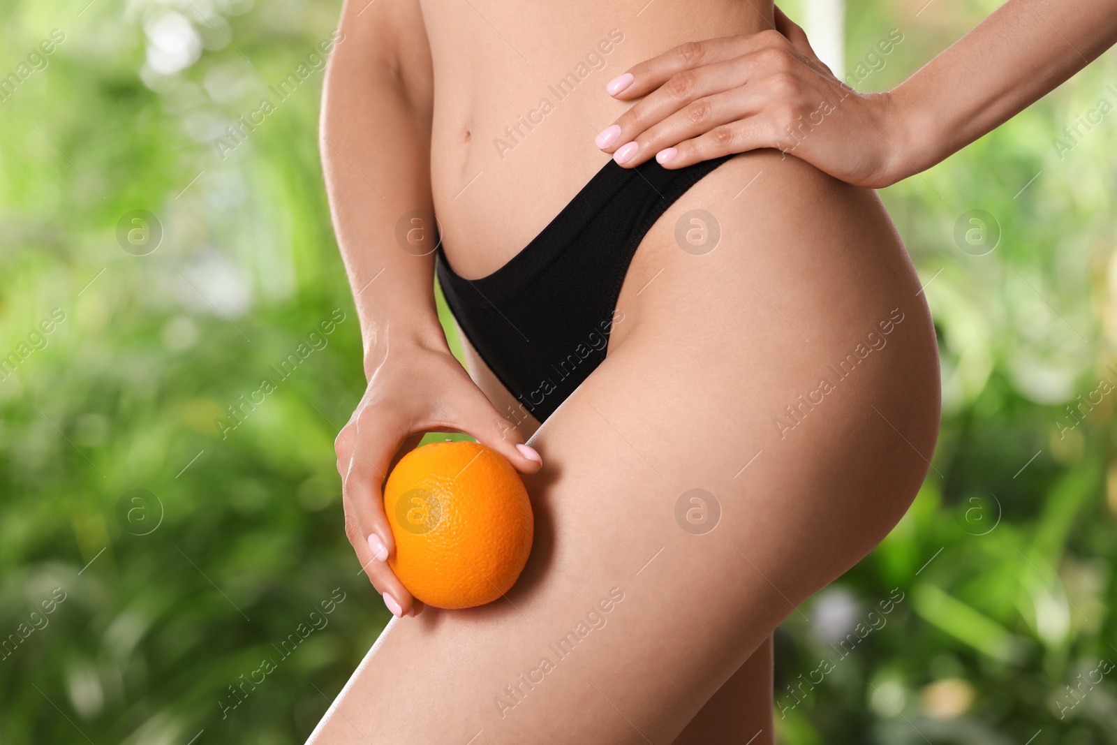 Photo of Closeup view of slim woman in underwear with orange on blurred green background. Cellulite problem concept