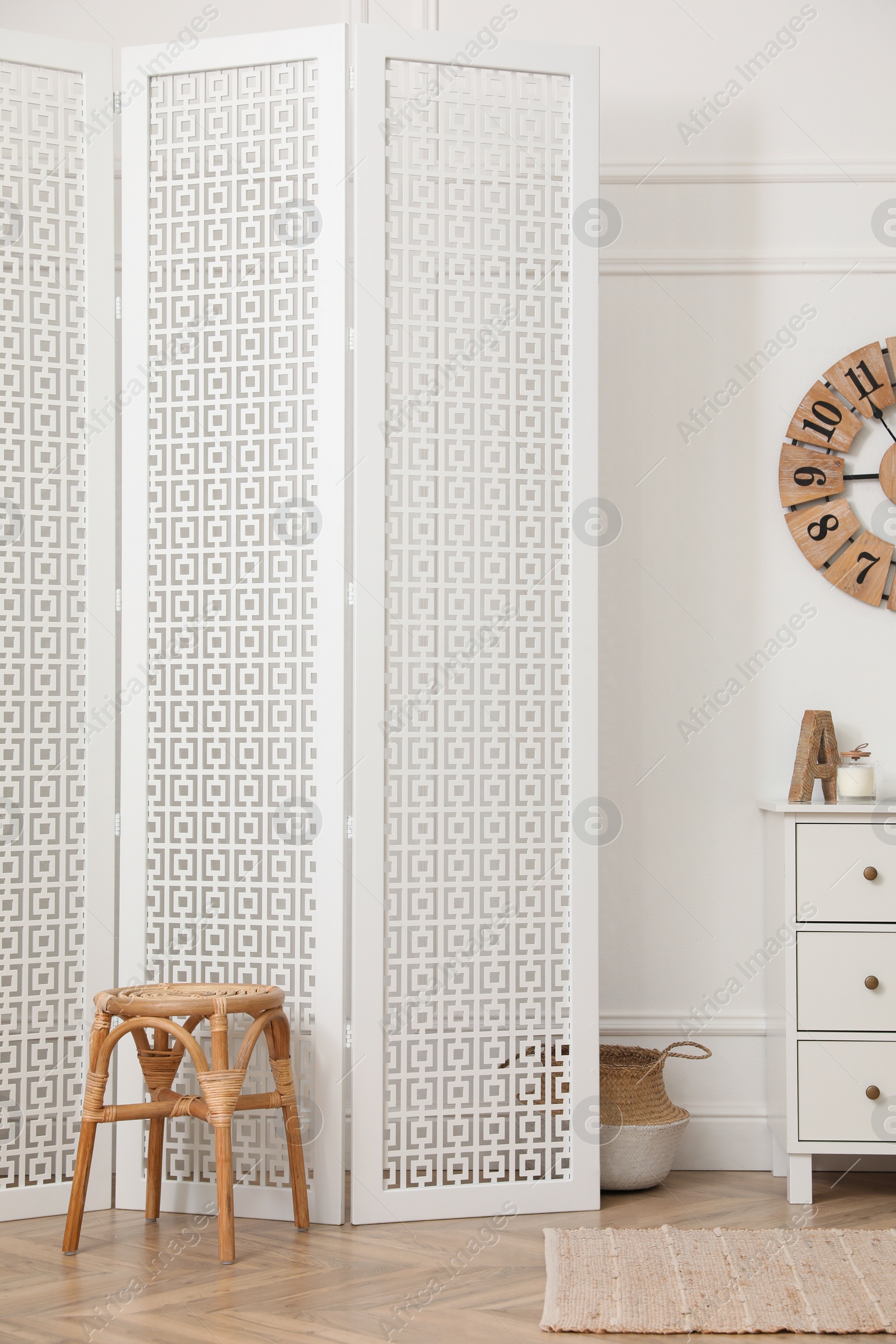 Photo of Stylish room with wooden folding screen and chest of drawers near white wall. Interior design